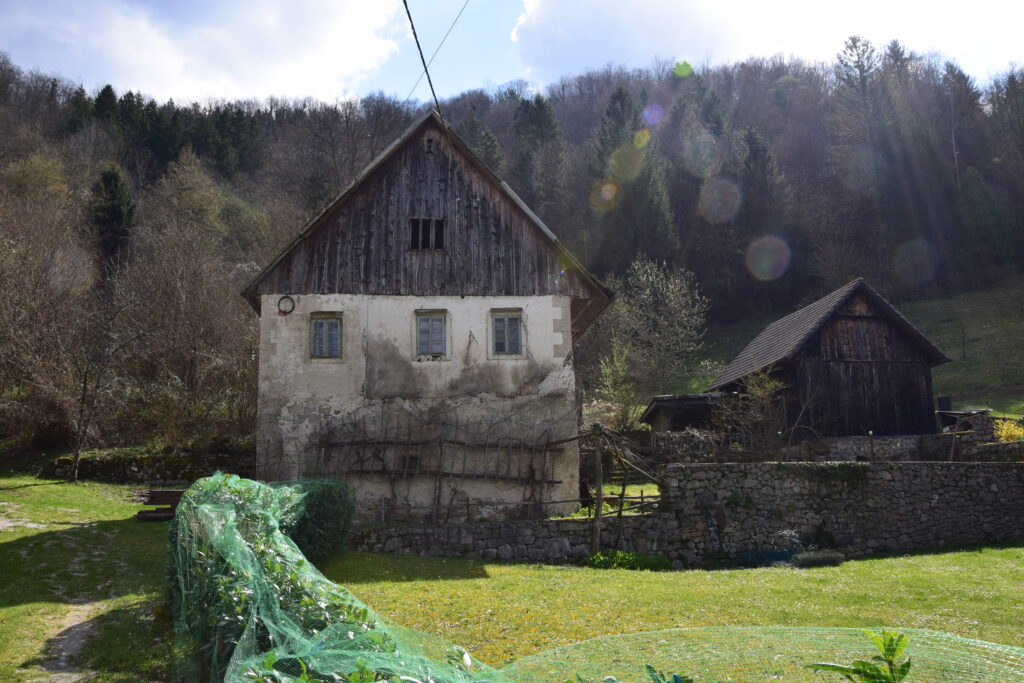 Slika prikazuje staro hišo v vasi Dečina. Je kamnita, podstrešni del je lesen, kritina pa je opečna.